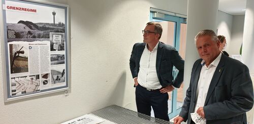Erster Kreisbeigeordneter Klaus-Peter Willsch und Prof. Dr. Andreas Rödder eröffnen die Plakat-Ausstellung „Die Mauer“ und schauen sich die Exponate von Achim Carius an, der ein Stück Berliner Mauer und Teile der Grenzzäune mitgebracht hatte.