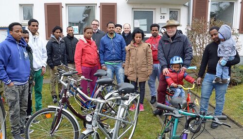 Axel Burisch (mit Hut) überreicht den Flüchtlingen in Idstein in Anwesenheit von Landrat Burkhard Albers (5. von rechts) und Idsteins Bürgermeister Christian Herfurth (7. von links) die ersten Fahrräder.