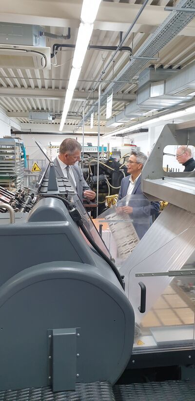 Auch die historische Heidelberger Druckmaschine ist noch im Einsatz, wie Geschäftsführerin Nicoletta Compagni Landrat Frank Kilian zeigt.